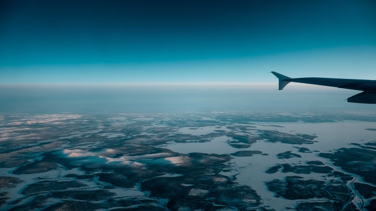 비행기 날개 아래로 눈 덮인 겨울 대지와 얼어붙은 호수가 펼쳐진 항공기 창밖 풍경